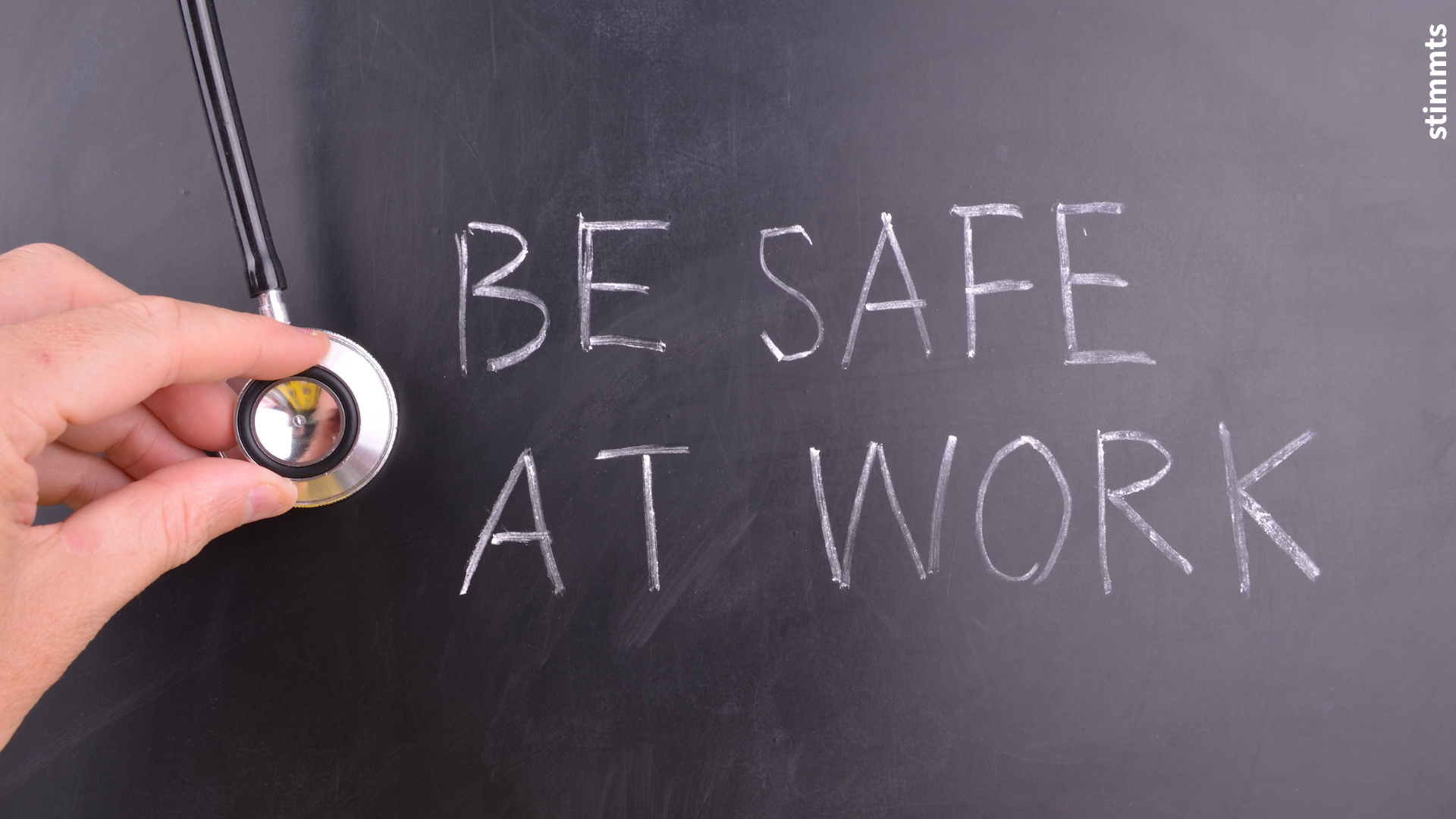BE SAFE AT WORK — Hand mit Stethoskop vor Tafel